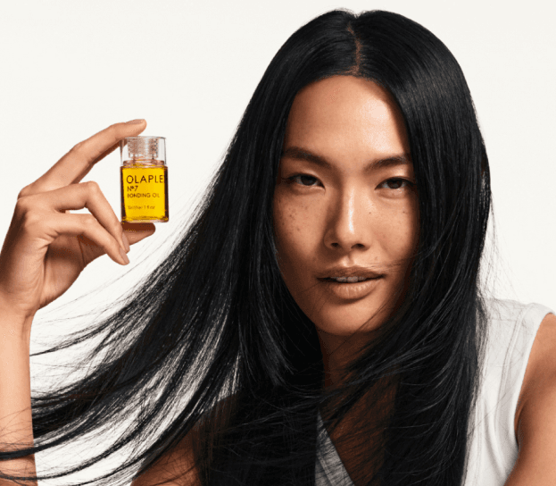 Model with long glossy hair holding a bottle of OLAPLEX Bonding Oil, a Glamsquad styling partner product